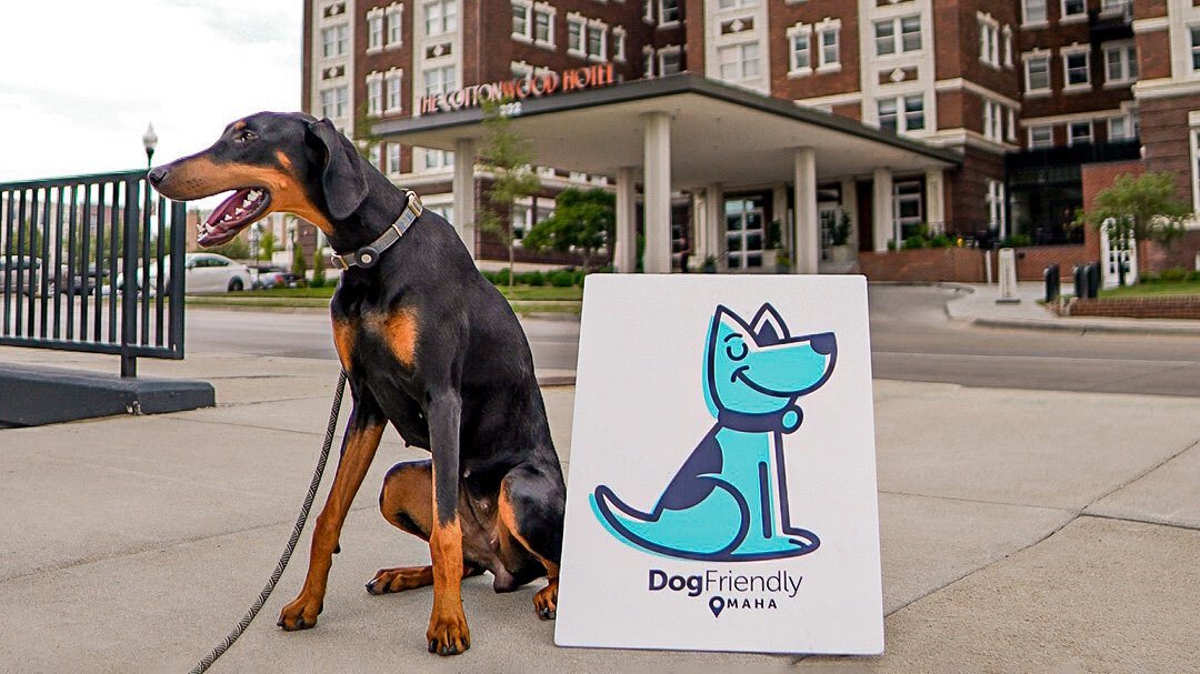 dog sitting next to the dog friendly omaha sign in front of the kimpton cottonwood hotel